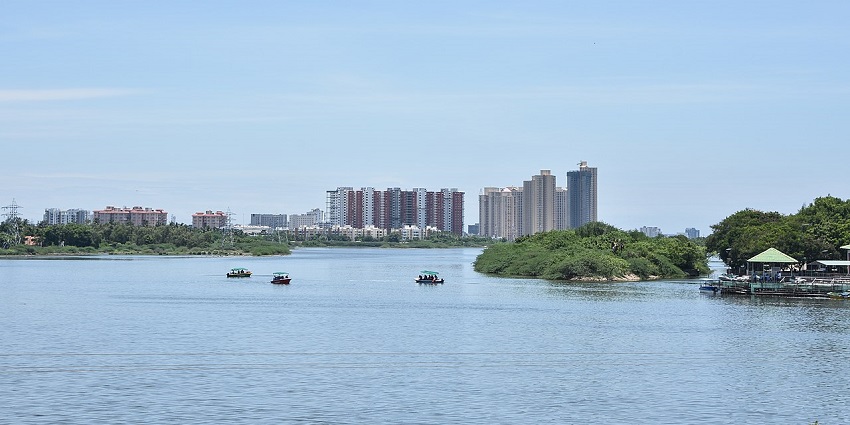 Boats sail on the calm Muttukadu Backwaters with city buildings in the distant skyline.