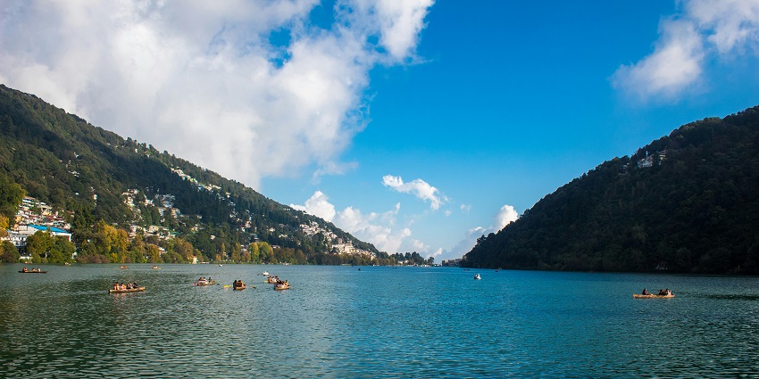 Scenic view of Nainital lake with colorful boats floating peacefully in the distance.
