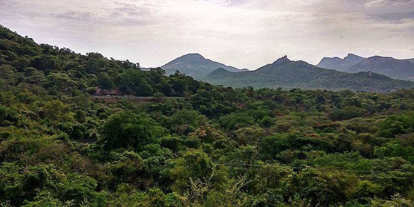 Namada chilume in Tumkuru with a distant road, railing, dense greenery, and mountains.