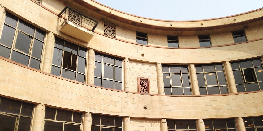Curved stone building with glass windows and lion statues at the entrance in daylight.

