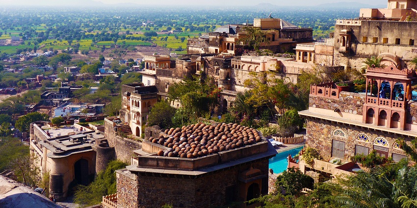 Ancient fort buildings with domed roofs overlooking lush green fields and the countryside, among the places to visit near Jaipur within 500 km.
