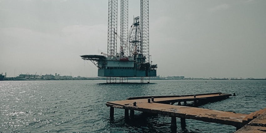 An oil platform stands near the sea in Baku, silhouetted against the horizon at sunset.
