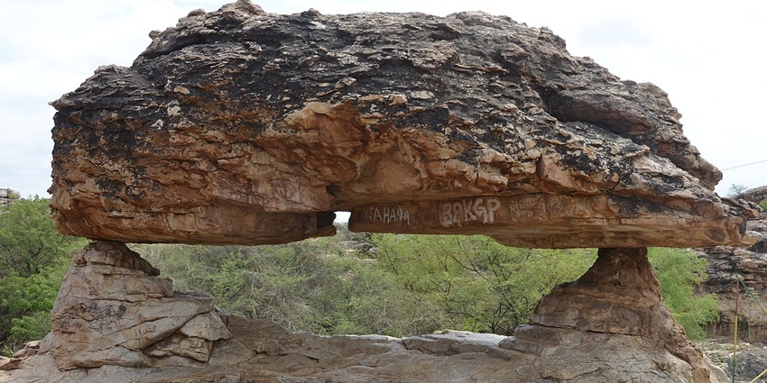 A balanced rock formation at Orvakal Rock Garden in Andhra Pradesh, with trees behind it.