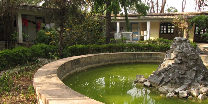 The circular stone pond surrounded by greenery at Osho Ashram with a rock fountain.