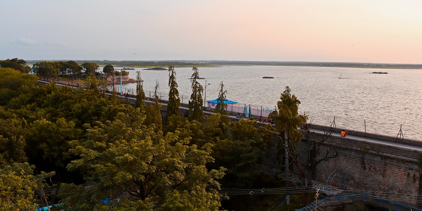 Sunset view over Osman Sagar with a tree-lined road and wall beside the water.