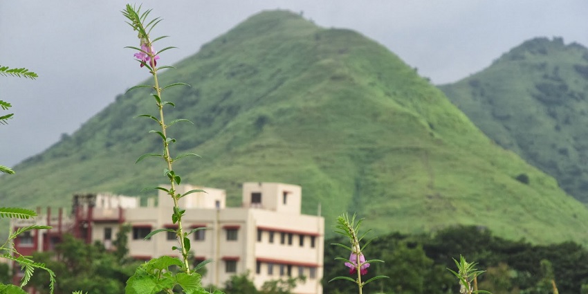 A glimpse of a green hill near Pandavkada Falls, with a few residential buildings at the base of the hill.