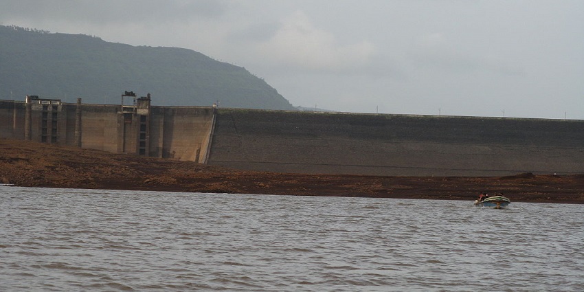 A distant view of Panshet Dam with a motor boat gliding past through its waters.