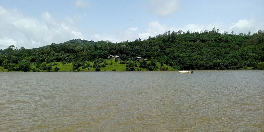 Panshet Dam in Pune with a large water body and boats under a clear sky.