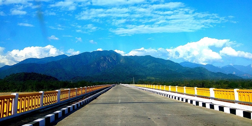 Pasighat Bridge with yellow railings and green mountains in the background.
