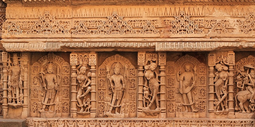 Intricately carved sandstone wall depicting deities, dancers, and decorative patterns