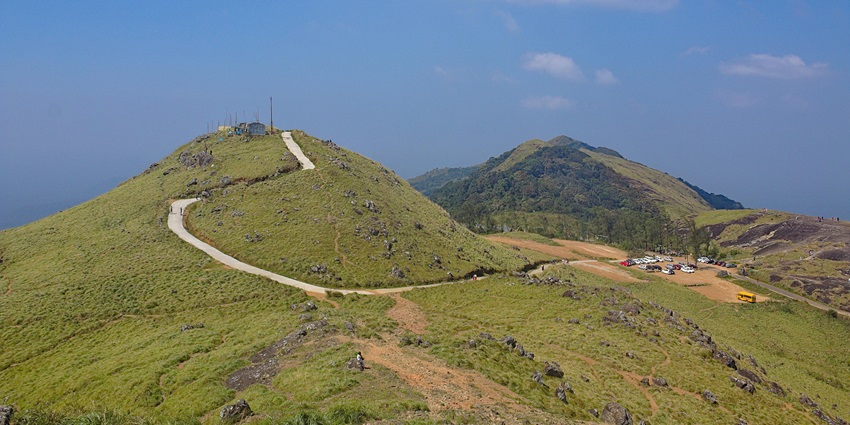A scenic view of Hills in Kerala, featuring mist-covered peaks, winding roads, and lush greenery.