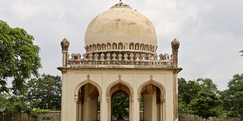 Dome-shaped, ornate Qutb Shahi tomb surrounded by greenery against a cloudy grey sky, one of the best places to visit near Gachibowli.