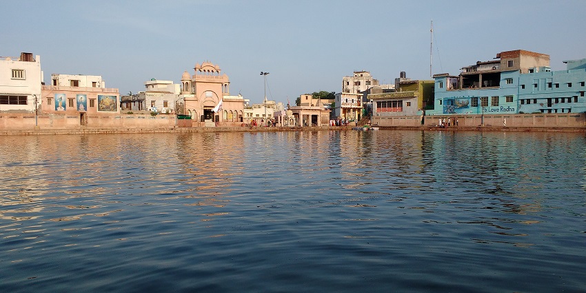 Radha Kund with a large water body and different buildings and structures surrounding it.
