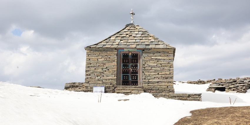 View of the stone temple surrounded by snow under a cloudy sky.