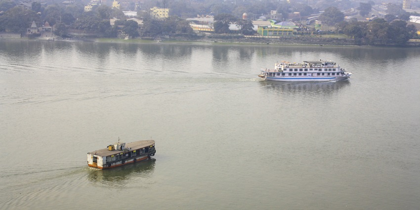 Two boats sail across a wide, calm river with a distant view of the city on the shore.