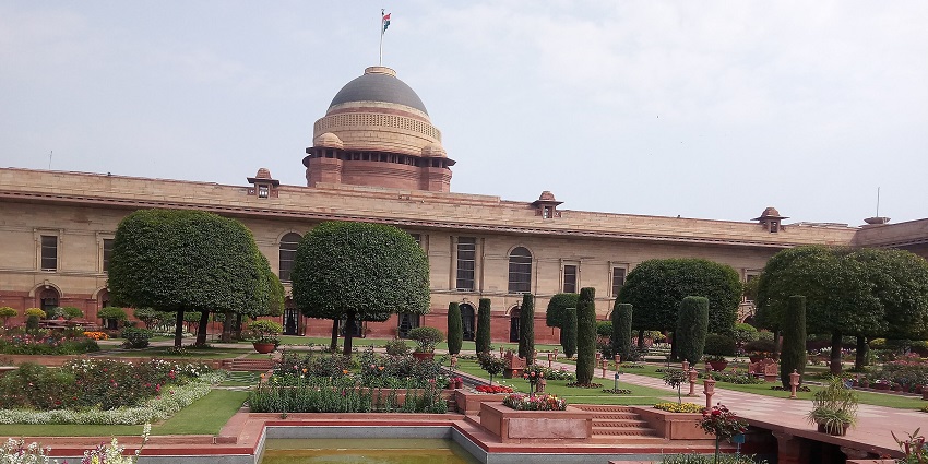 Lush formal garden with trimmed trees, colorful flowers, pathways, and water features near Janpath Market places.
