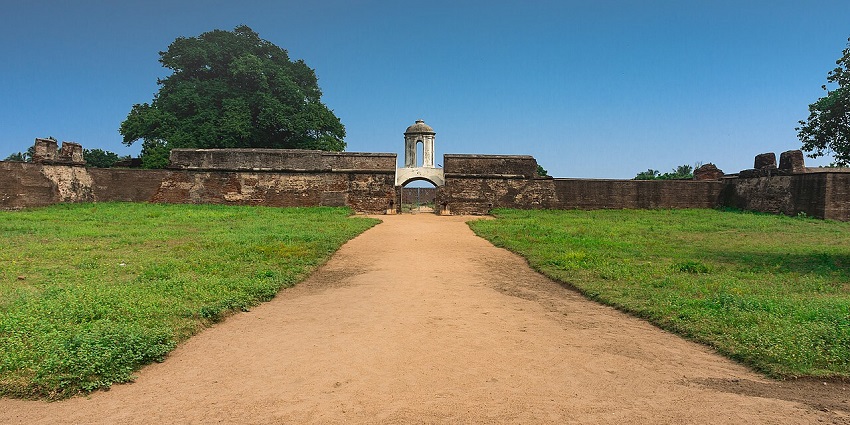 A wide sandy path leads to the main entrance of a historic stone fort under a clear blue sky.