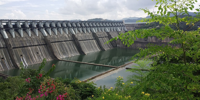 Sardar Sarovar Dam in Gujarat with calm water body, closed doors of the dam and greenery.
