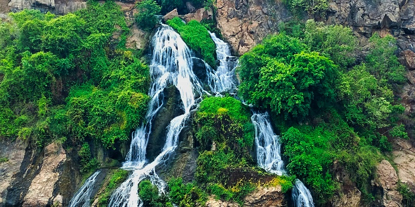 Scenic view of Sathodi Falls surrounded by lush greenery and rocky terrain.
