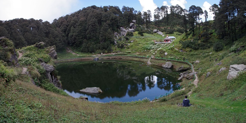 Serene hilltop lake surrounded by dense forest with a small temple in the distance