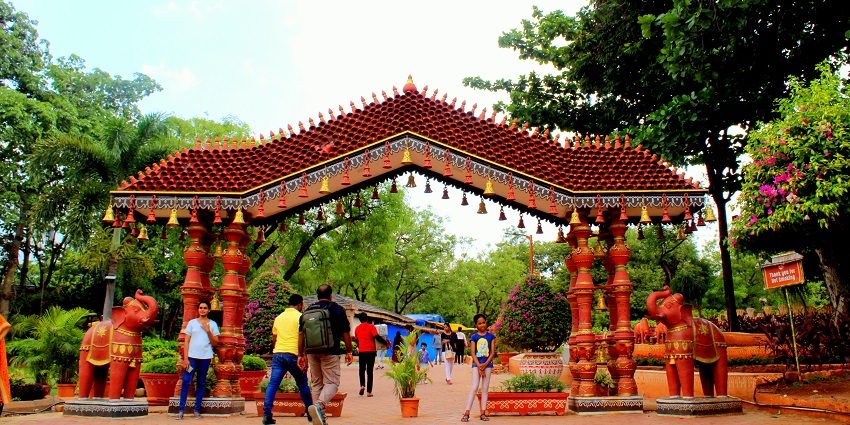 Visitors walk under the ornate red entrance arch at Shilparamam, surrounded by greenery, one of the best places to visit near Gachibowli.