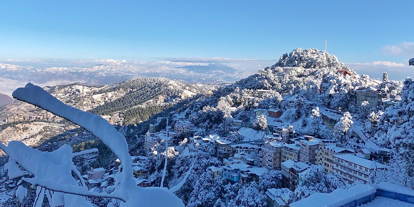Snow-covered hills and houses in Shimla under blue sky are top places to visit near Chandigarh in winters.