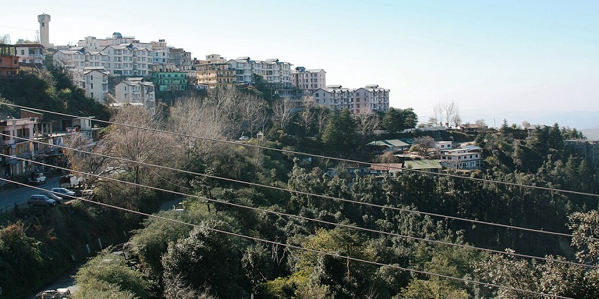 View of Shoghi town with clustered buildings enclosed by hilly terrain and dense greens