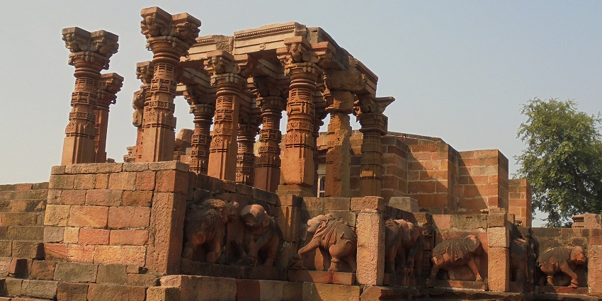 An ancient stone temple with carved pillars and elephant sculptures on a raised platform.
