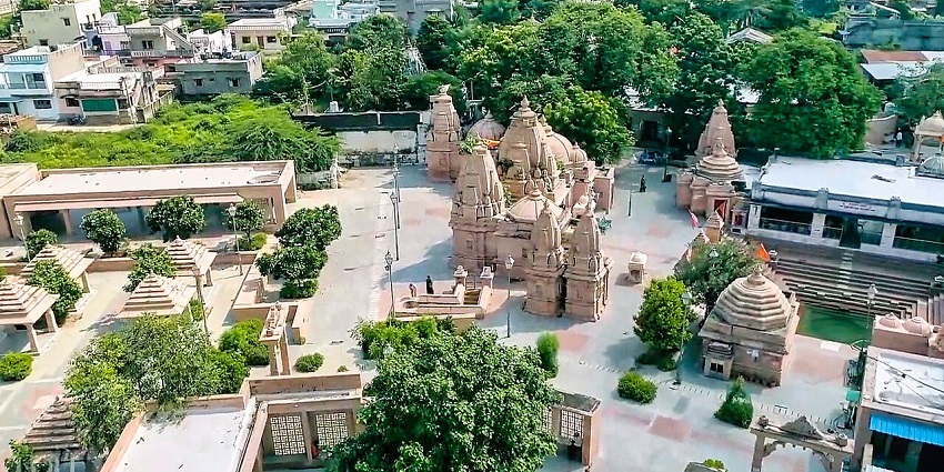 Aerial view of temple complex with ornate spires, landscaped pathways, and cityscape.
