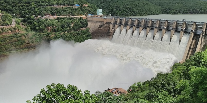 Large dam with water reservoir and surrounding landscape under a clear sky.