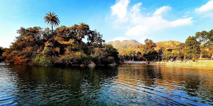 Mount Abu lake is surrounded by lush greenery and distant scenic hill views.