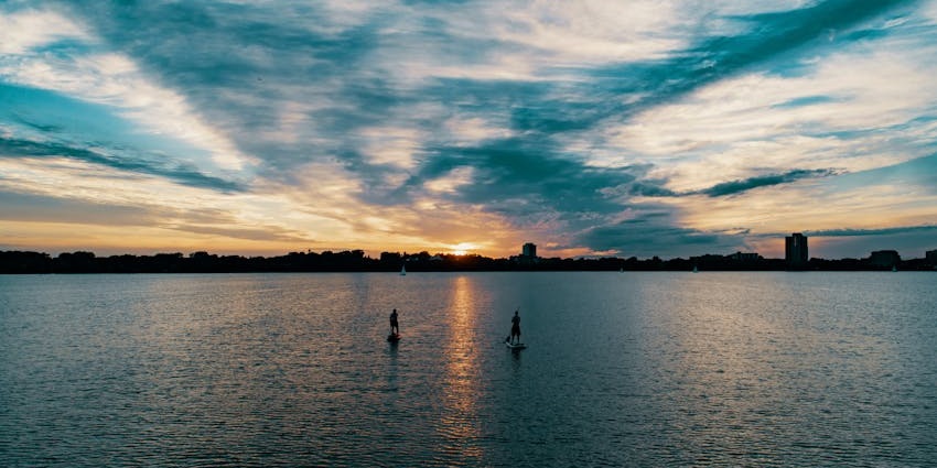 Distant two people paddleboarding on a large water body under a vibrant cloudy sky
