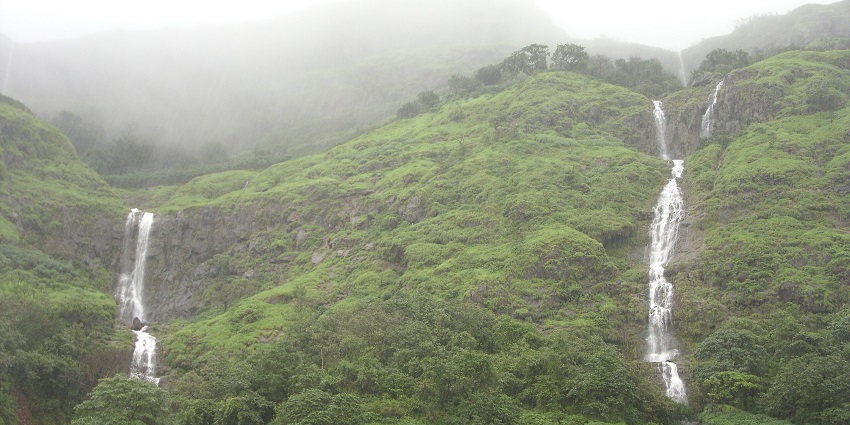 Multiple narrow waterfalls cascading down a green hillside under misty weather conditions, one of the best places to visit near Pune in monsoon for couples.