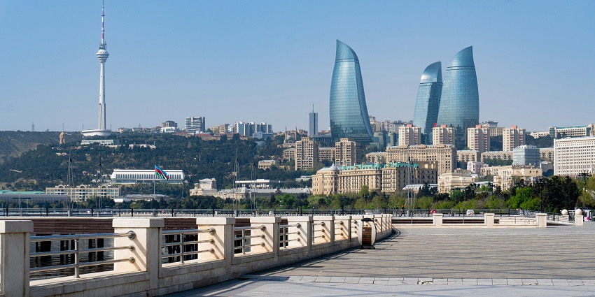 Caspian Waterfront promenade with city skyline and calm water under clear skies.
