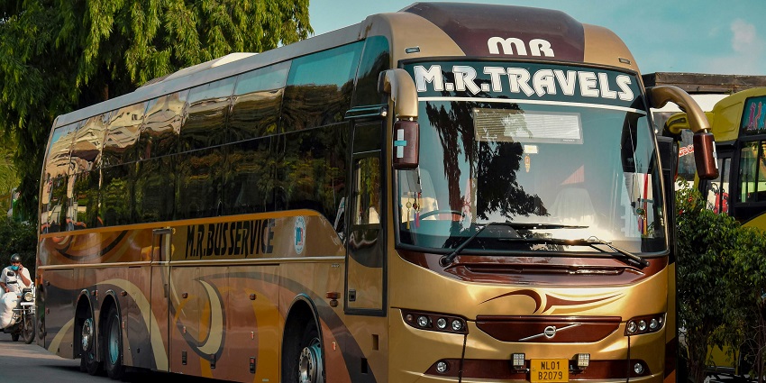 Image of a bus parked at a roadside stop with surrounding greenery and clear skies.