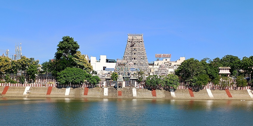 The towering gopuram of a temple is visible from across a pond in front of the temple