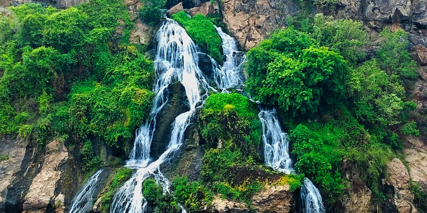 Water cascading over rocks at Thottikallu Falls is surrounded by lush green trees.