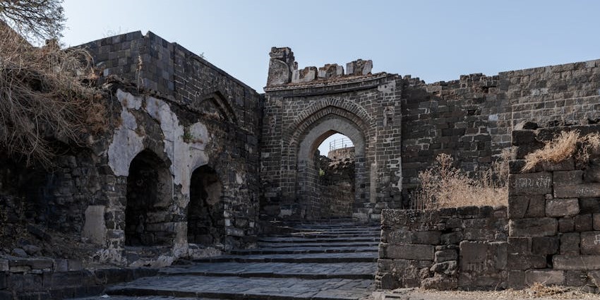 Stone steps and ancient walls of Tikona Fort surrounded by greenery.
