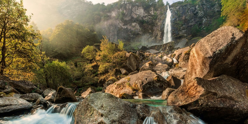 A scenic waterfall flows over wide rocky cliffs amid lush green forest, one of the best places to visit near Indore in July.
