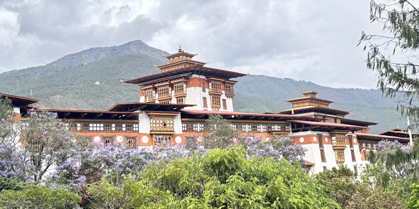 Traditional Bhutanese dzong with lush greenery and mountains in the background.