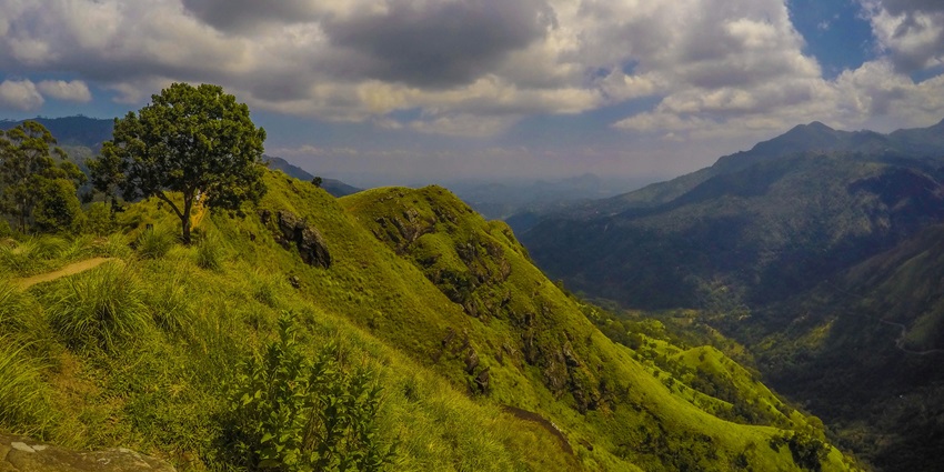 Green hills of Mandaragiri with rocky paths and scattered trees under a partly cloudy sky.
