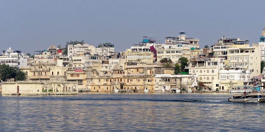 Beautiful lakeside view with Heritage buildings in a cluster and a boat gliding through the waters.
