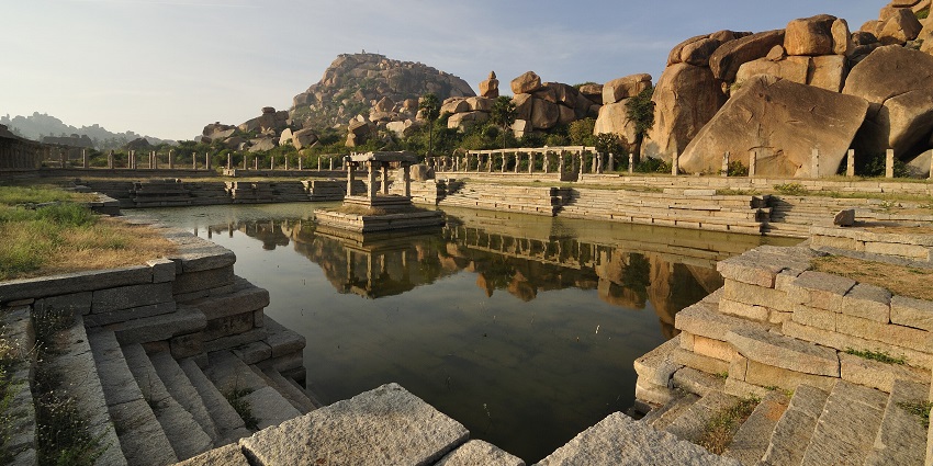 A wide view of the ruins of an ancient temple with a partially dried bath in Karnataka.