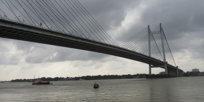 Modern cable-stayed bridge stretches over a wide river under a sky with boats below.