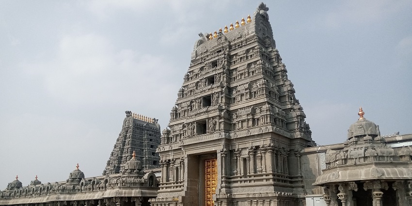 Intricately carved stone temple with a tall tower and golden door under a partly cloudy sky.
