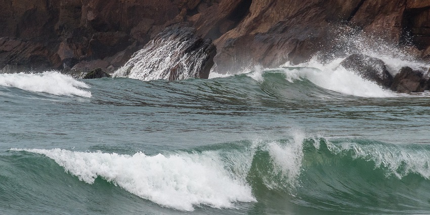 Waves crashing against rocky cliffs with splashes under cloudy sky and rough sea, one of the best places to visit near Vizag for 3 days.