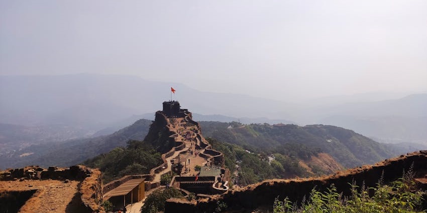 Ruins of Yellur Fort atop a rocky hill surrounded by natural greenery and open skies.
