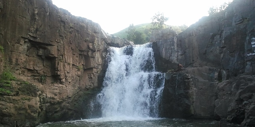 Zarwani waterfall in Shoolpaneshwar wildlife sanctuary with water flowing on the uneven rocky surface.
