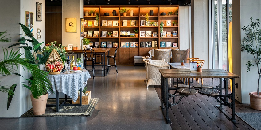 Warmly lit restaurant with wooden tables, chairs and a wall-mounted bookshelf.