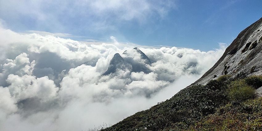 View from Agasthyarkoodam mountain top showing clouds and surrounding mountain peaks.